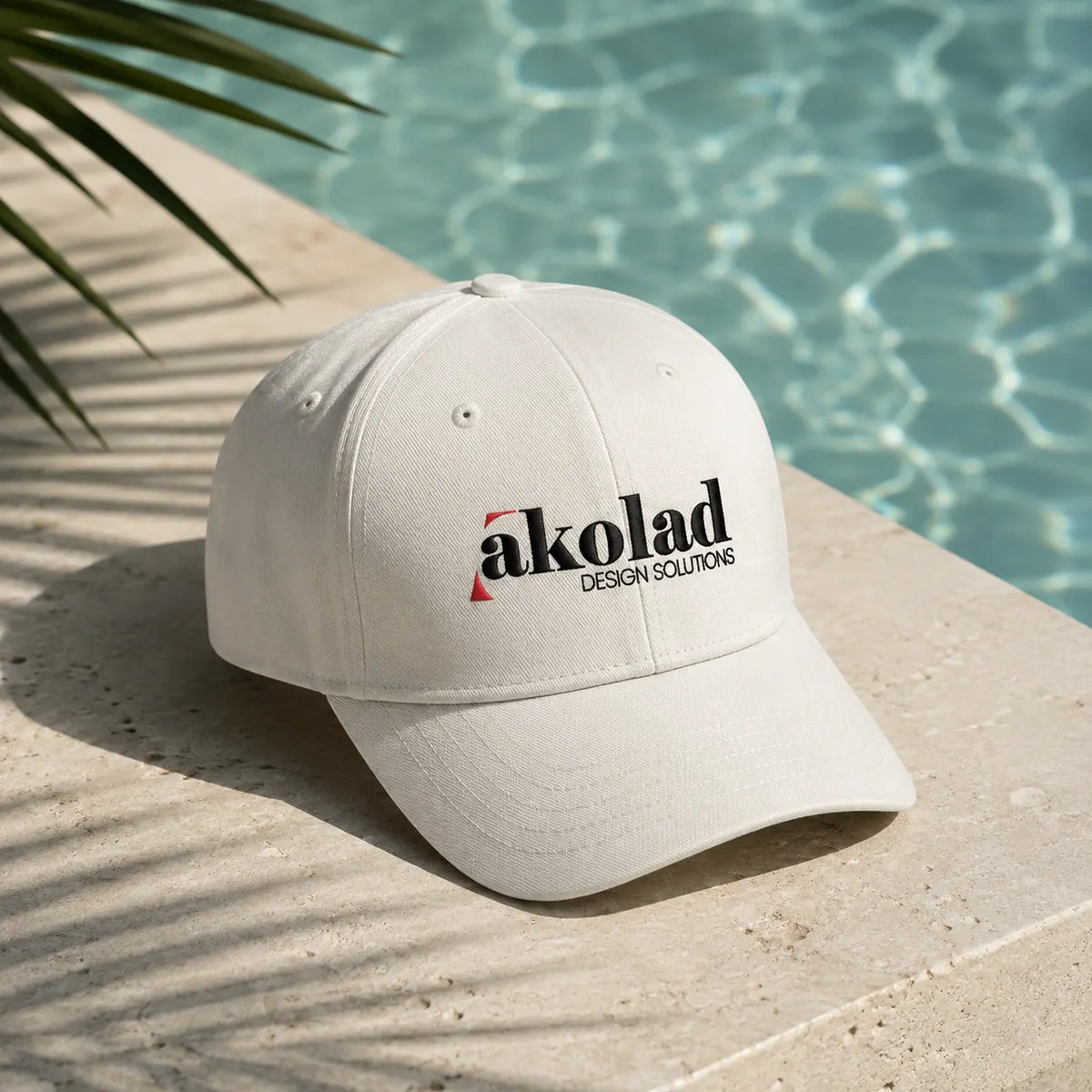 An embroidered cap in soft stone cotton resting on a poolside ledge.