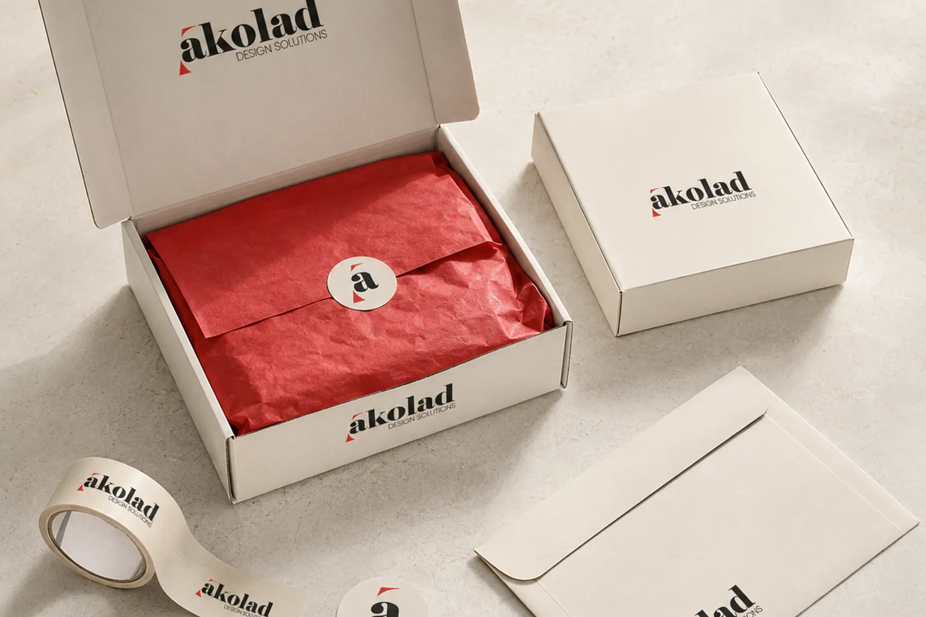 Branded shipping boxes, tissue paper, tape and a seal sticker photographed on a pale surface.